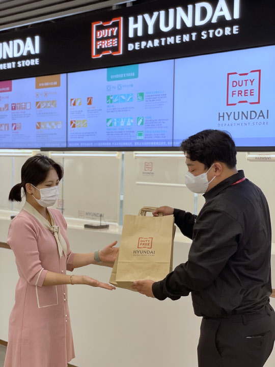 인천국제공항 현대백화점면세점 인도장에서 직원이 고객에게 면세품을 종이봉투에 담아 전달하고 있다. 현대백화점면세점 제공